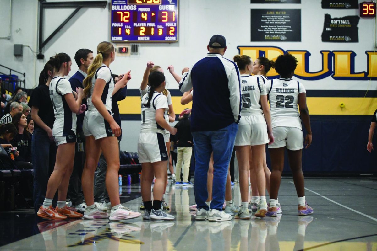 The varsity girls come together with coaches Shawn Stinson and Matt Boase during a timeout on Jan. 13 against Corvallis High School.